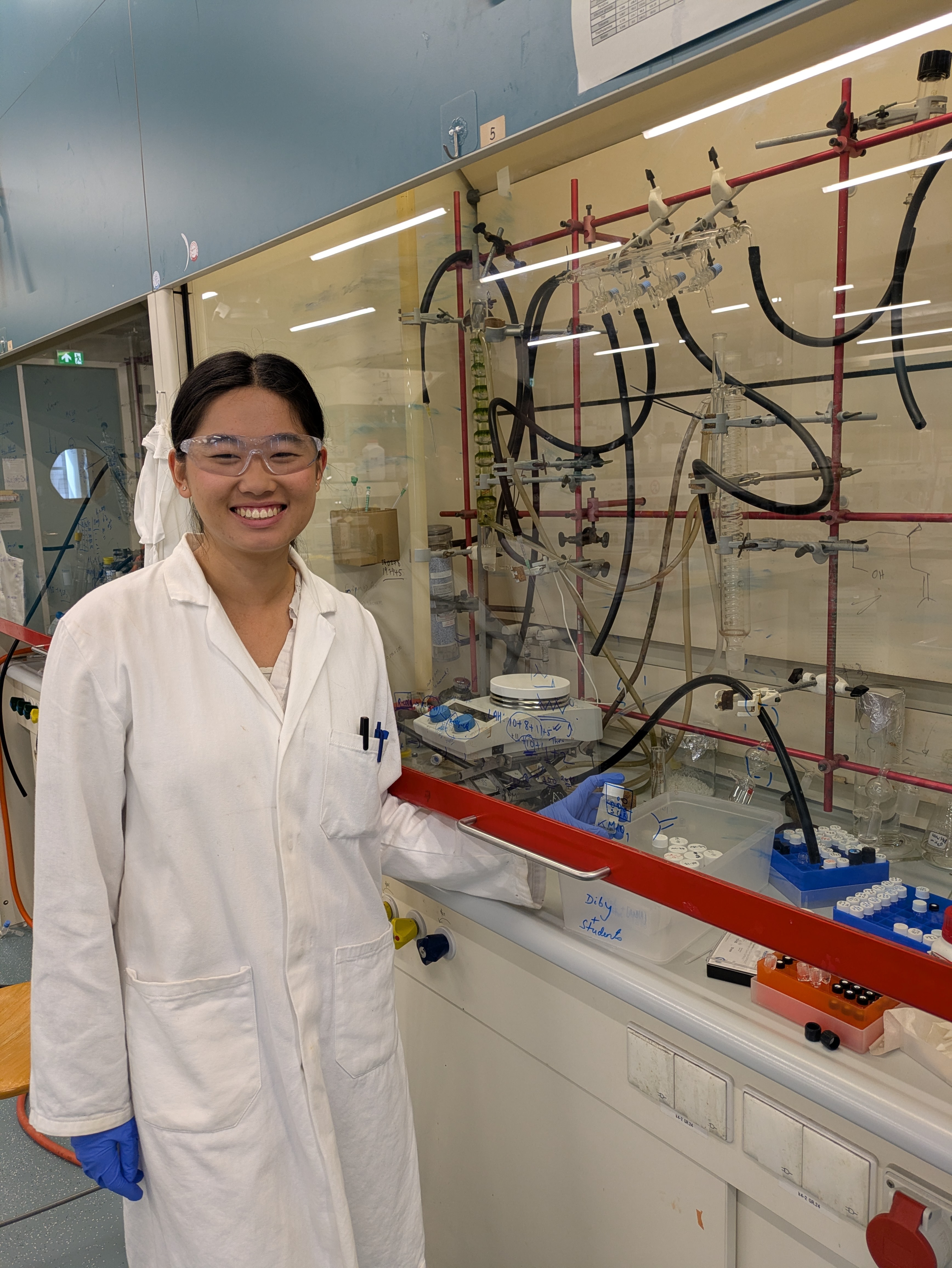 Anna standing beside lab instrumentation in PPE gear.